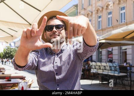 Man in sunglasses and sun hat framing with hands, finger frame. Stock Photo