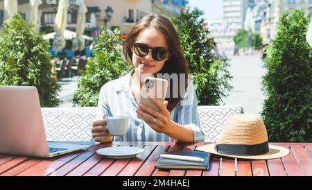 Young woman using smartphone while sitting in outdoor cafe in the city. Stock Photo
