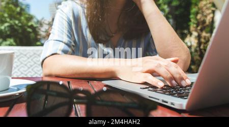 Female person using her laptop while sitting outdoor cafe in summer. Stock Photo
