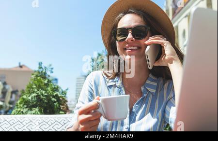 Woman in sunglasses and sun straw hat talking on the mobile phone while sitting in outdoor cafe. Stock Photo