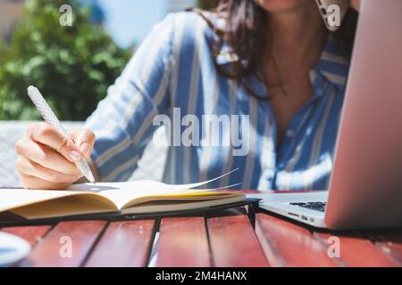 Female person writing notes in notebook while sitting outdoor cafe in summer. Stock Photo