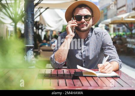 Man calling on mobile phone sitting in outdoor cafe. Stock Photo