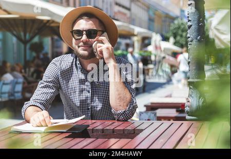 Man calling on mobile phone sitting in outdoor cafe. Stock Photo