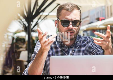 Man in sunglasses video chatting using his laptop outdoors. Stock Photo