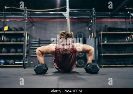 Portrait of a man doing push-ups using dumbbells in a gym Stock Photo