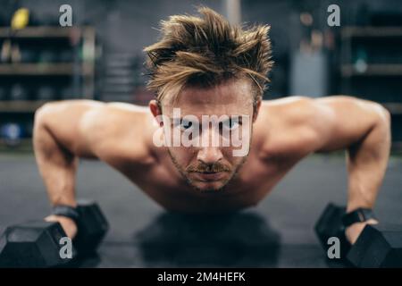 Close up photo of a strong man doing push-ups using dumbbells in a gym Stock Photo