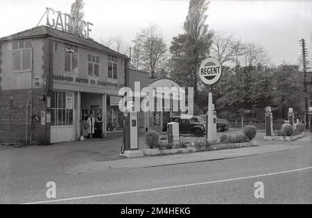 1950s, historical, exterior of a garage of the era, the Hargood Motor Co, with Regent Petrol pumps on the forecourt, on Wilmslow Rd, Didsbury, Manchester, England, UK. A man and woman can be seen standing at the entrance to the garage, which has its name Hargood Motor Co (Parrs wood) Ltd written on the exterior of the building.  Beside the garage, on the right, a sign for Hargood Motor Sales, with cars of the era parked outside. In this era, regular evening motor auctions were held at the site located within the city of Manchester. Stock Photo