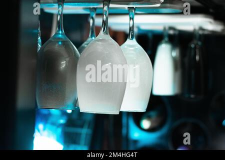 white wine glasses hanging over the top, in a liquor cabinet in a bar, with an ambiance of blue light on a black background. Stock Photo