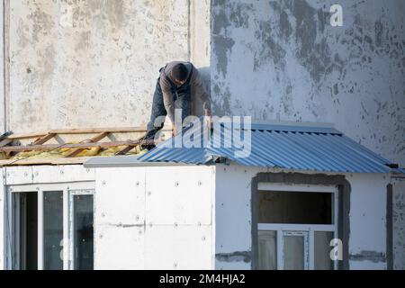 Tiraspol, Moldova - December 13, 2022: Builder covers roof with corrugated aluminum sheet. Worker are building on frame roof for balcony at december. Stock Photo