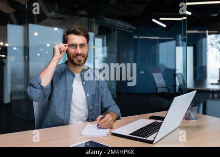 Portrait of successful businessman behind paper work, man in shirt smiling and looking at camera, financier boss inside office using laptop in work at workplace. Stock Photo