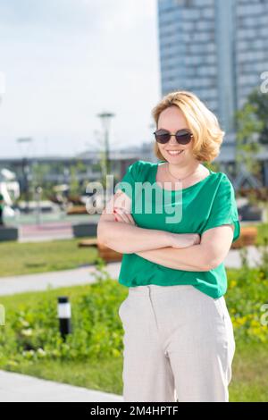 Portrait of a smiling happy middle-aged woman in sunglasses walking through the streets of the city, vertical frame. A beautiful student girl illumina Stock Photo