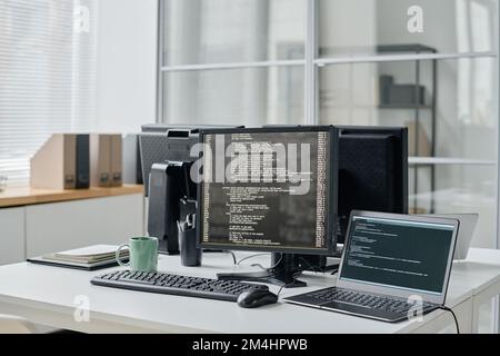 Horizontal image of workplace of programmer with computer monitors with codes on screens standing on table Stock Photo