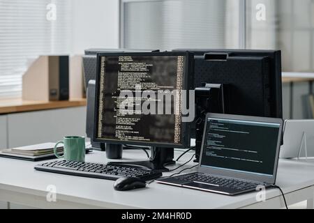 Workplace of developer with computer and laptop with codes on screens in modern office Stock Photo