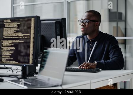 African American young developer in eyeglasses concentrating on his online work on computer sitting at workplace Stock Photo