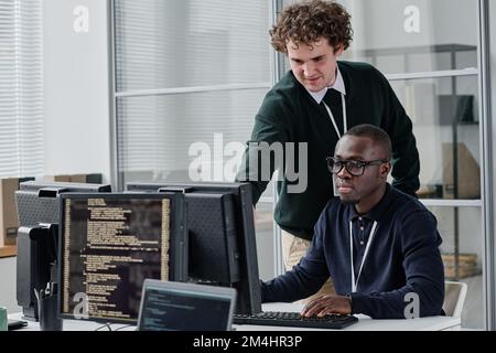 Two young colleagues discussing new program codes on computer during work in modern office Stock Photo