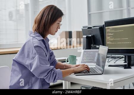 Asian young woman writing codes on laptop while working at her workplace in office Stock Photo