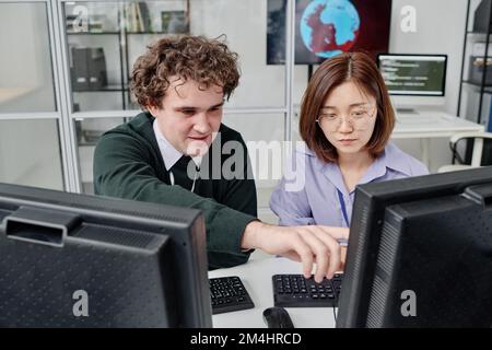 Two young colleagues working with security of computer program together, they sitting at table with computer monitors Stock Photo