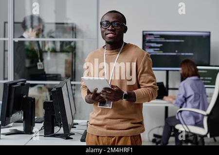 Portrait of African American IT specialist in eyeglasses smiling at camera while working online on digital tablet Stock Photo