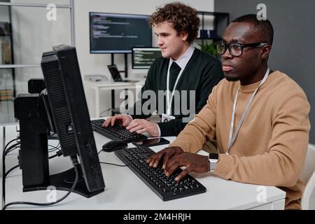 Two programmers sitting in front of computer monitors and writing security code for program Stock Photo