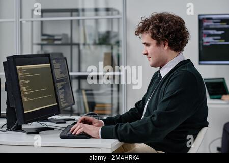 Young IT specialist writing codes for program on computer while sitting at his workplace in IT office Stock Photo