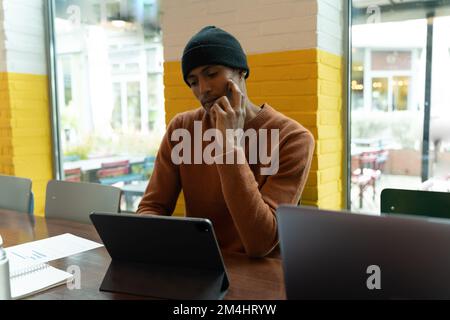 Young man working in a co-working space. Focused man looking at the tablet. Notes and a writing pad on the table. Yellow and white painted wall with g Stock Photo