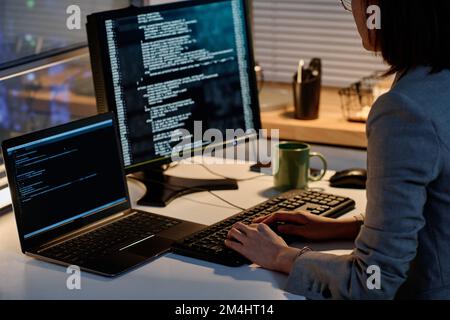Close-up of female programmer working with security codes on computer sitting at her workplace in dark office Stock Photo