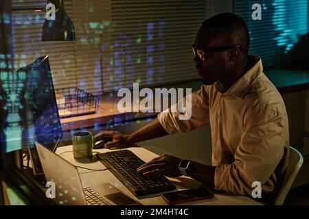 African American businessman typing keyboard security codes on computer while working overtime in office Stock Photo