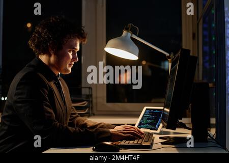 Young programmer writing codes on computer to develop new software, he working overtime in office Stock Photo