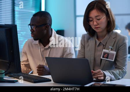 Two young colleagues sitting at table and working on computers with computer program Stock Photo