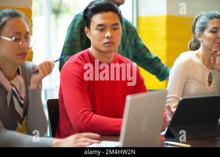 A group of people working together as a team on a project in a co-working space. Multiracial people. Looking at the laptop in front of them on the woo Stock Photo