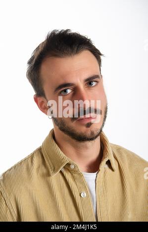 Closeup of a portrait of a young Caucasian man with serious expression and deep look from blue eyes looking in the room. Face with beard, mustache and Stock Photo