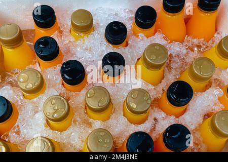 Orange juice or lemonade bottles in a box of ice, close up. Stock Photo