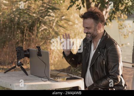 Man greeting through laptop webcam, connecting to the internet outdoors surrounded by nature at sunset Stock Photo
