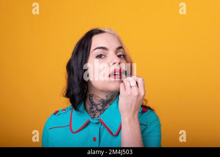 Beautiful caucasian woman applying a bright red color lipstick on her lips over yellow background Stock Photo