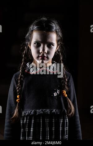 Little girl disguised from Wednesday Addams to celebrate Halloween party. Dark background Stock Photo