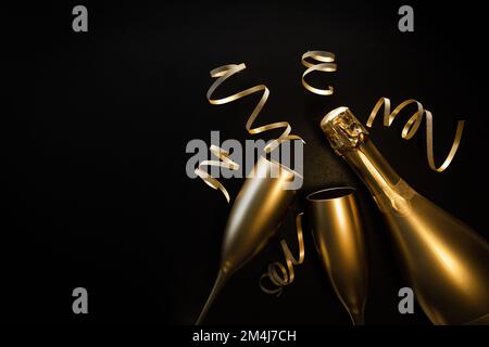 golden champagne bottle and two glasses with ribbons on black background with copy space. new year eve and anniversary celebration Stock Photo