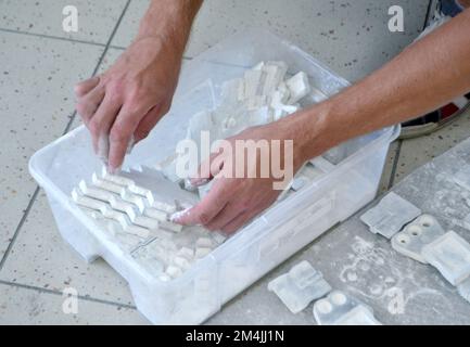 Male worker sorts through models in hands, lying in box and covered with white polyamide powder close-up. Objects printed on powder 3D printer. Technology Multi Jet Fusion MJF. 3D printing technology Stock Photo