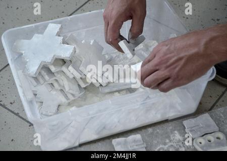 Male worker sorts through models in hands, lying in box and covered with white polyamide powder close-up. Objects printed on powder 3D printer. Technology Multi Jet Fusion MJF. 3D printing technology Stock Photo