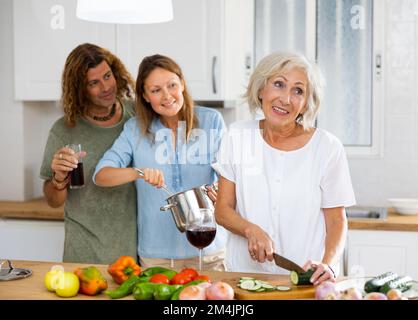 Joyful old female cutting vegetables during man and women drinking wine at the modern cuisine Stock Photo