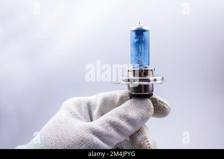 Old, broken, car bulb, H4, blue, broken in the hand on a gray background Stock Photo