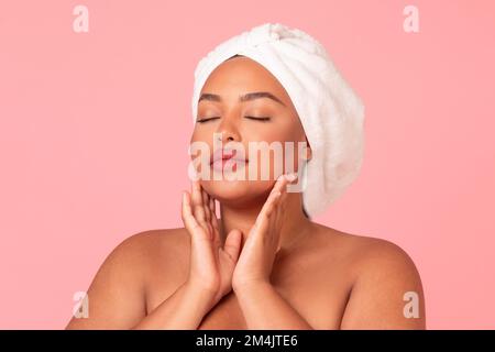 Portrait of body positive black woman with smooth skin touching her face while posing over pink studio background Stock Photo