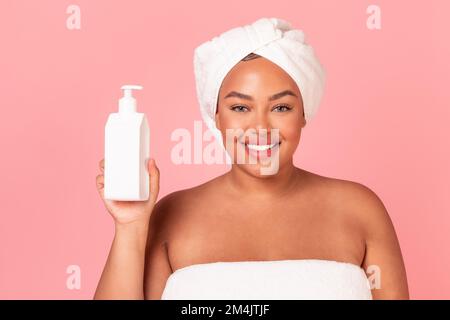 Attractive african american plus size lady with bottle of moisturising body lotion, posing over pink background Stock Photo