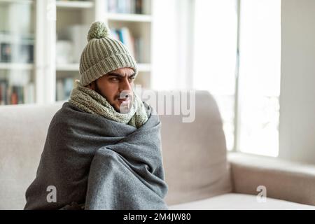 Freezing middle eastern guy sitting on couch in living room Stock Photo