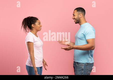 Side view of excited african american friends man and woman spreading hands and talking, pink background Stock Photo