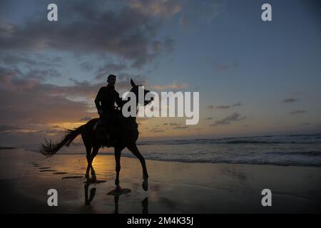 Palestinian man rides his horse along the beach at sunset in  Gaza City. Stock Photo