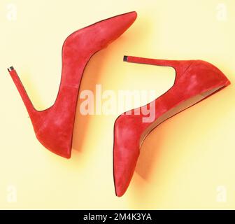Footwear with thin high heels, stiletto shoes, top view. Shoes made out of red suede on yellow background. Pair of fashionable high heeled pump shoes Stock Photo