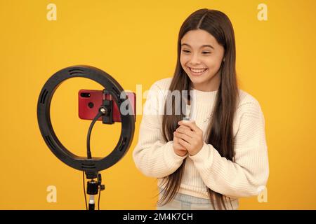 Beauty blog. Blogging, videoblog. Teenager child blogger with phone recording video on isolated yellow studio background. Influencer teen girl Stock Photo