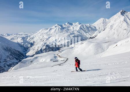 Spotrsman woman snowboarder freerider rides down from top of ridge in a big mountains, winter freeride extreme sport Stock Photo