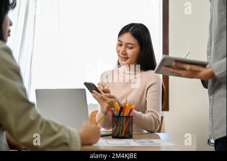 Professional millennial Asian female developers working with her colleagues on a new mobile application prototype. Stock Photo