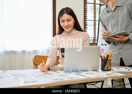 Attractive and professional millennial Asian male and female developers are in the meeting room, working together on their new mobile application prot Stock Photo
